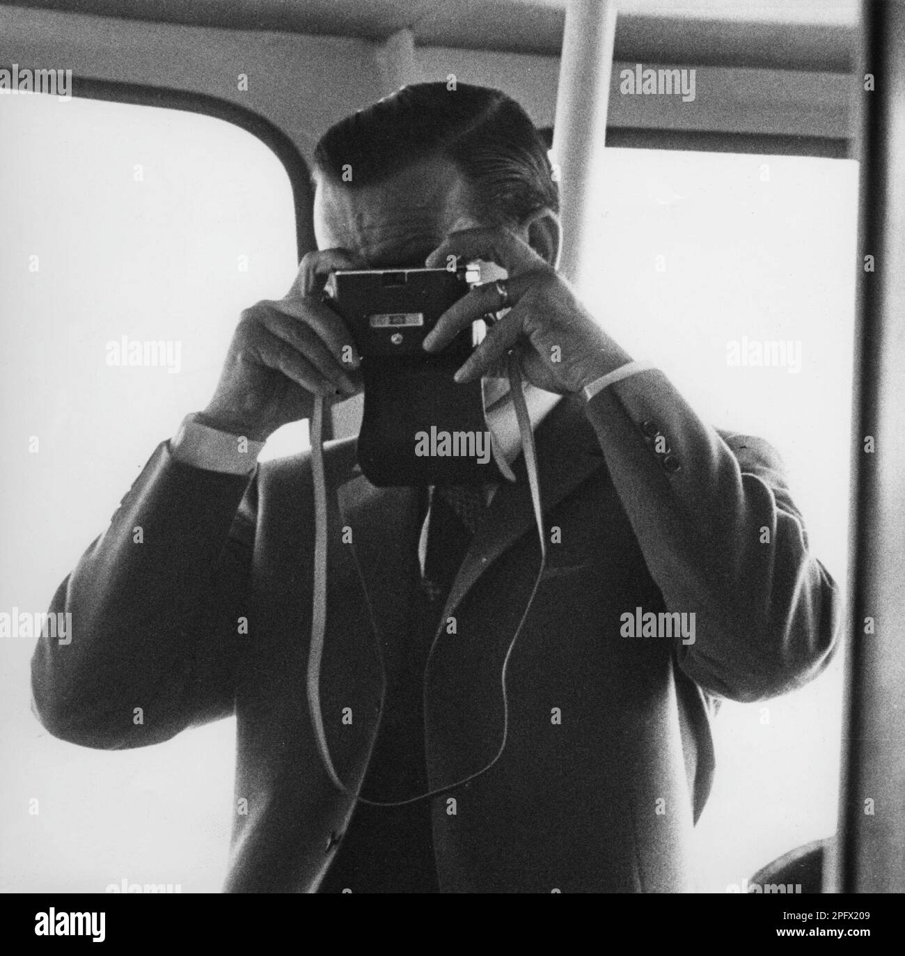 Amateurfotograf in den 1960er. So sehr ein Amateur, dass er seine Kamera falsch herum hält und in das Objektiv auf der Vorderseite schaut, anstatt in den Sucher auf der Rückseite der Kamera. Damit macht er ein Foto von sich selbst. Schweden 1967 Stockfoto