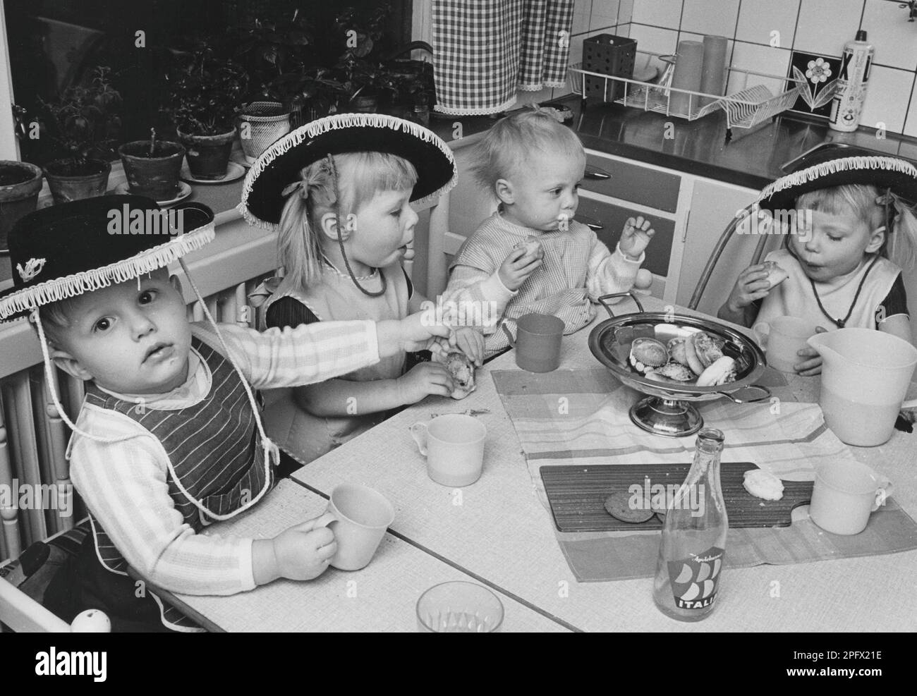 Kinder im 1960er. Jahrhundert. Vier Mädchen und Jungen in Hüten sitzen am Küchentisch und genießen Limonade, Kekse und Brötchen. Schweden 1965 Stockfoto