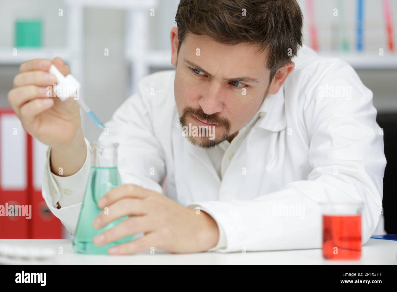 Der Wissenschaftler gibt blaue Flüssigkeit in einen erlenmeyerkolben Stockfoto