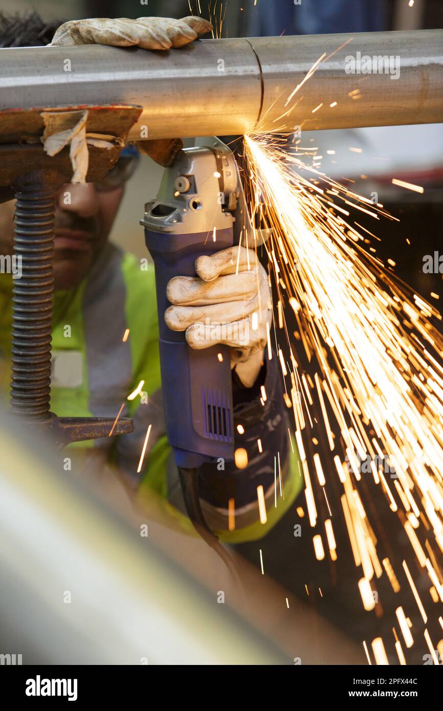 Schwerindustriearbeiter, der Stahlrohre mit Winkelschleifer schneidet Stockfoto