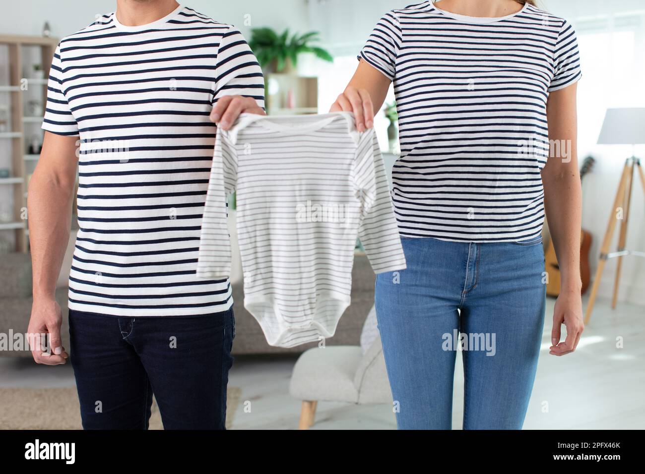 Glückliche zukünftige Eltern zeigen Babykleidung Stockfoto