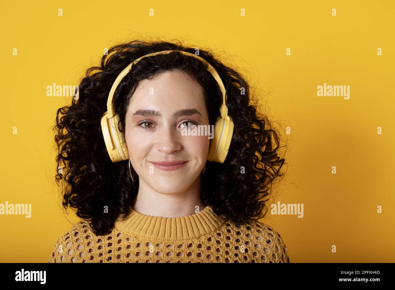 Ein weißes Mädchen mit gelbem Hintergrund und lockigen Haaren, das auf die Kamera schaut Stockfoto