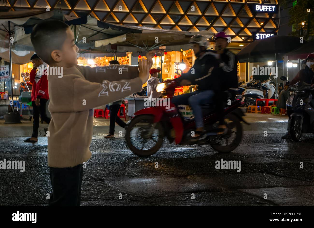 Ein Junge steht mit ausgestreckten Armen auf der Straße auf dem Nachtmarkt in Dalat, Vietnam. Stockfoto
