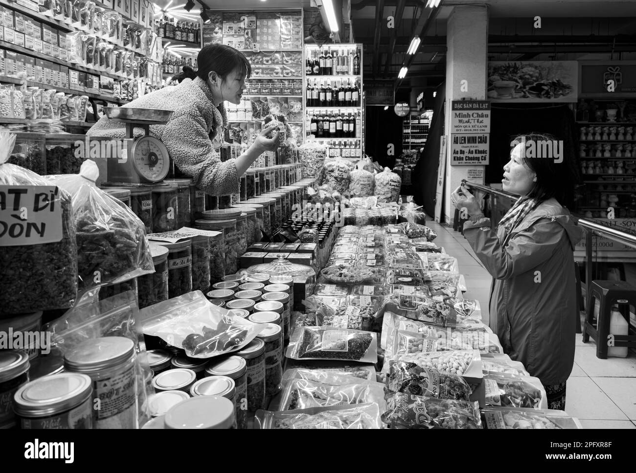 Eine vietnamesische Kundin mittleren Alters unterhält sich mit einer jungen Frau, die einen Verkaufsstand betreibt und lokale Spezialitäten im Dalat Market, Vietnam, verkauft. Stockfoto