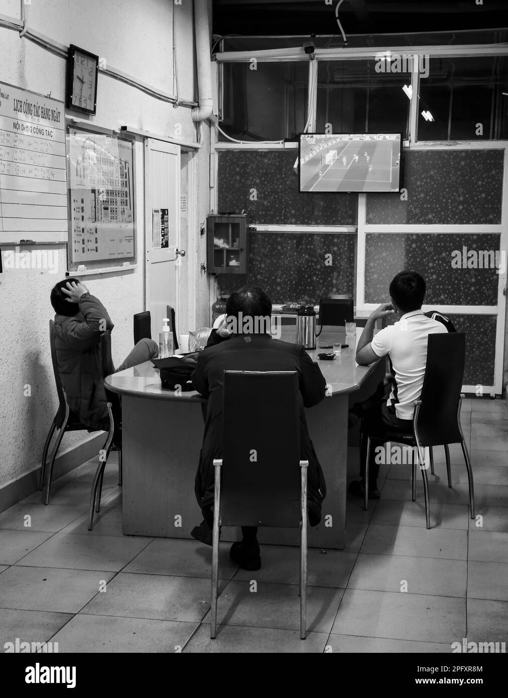 Drei Sicherheitsleute auf dem Dalat Market in Vietnam schauen sich ein Fußballspiel im Fernsehen an, das bei der FIFA-Weltmeisterschaft 2022 stattfindet. Stockfoto