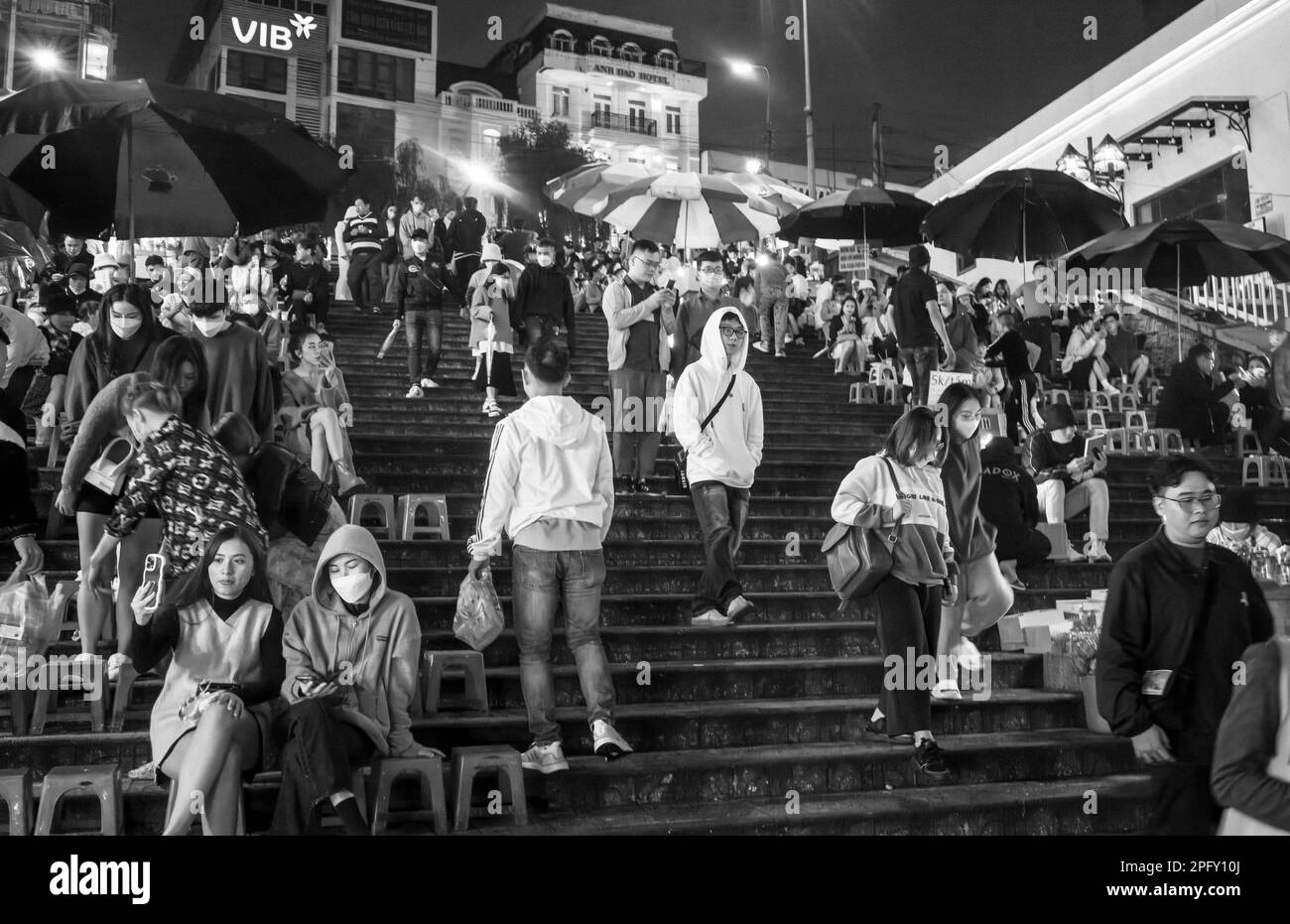 Junge Vietnamesen treffen sich mit Freunden, um auf Treppen mit Blick auf den Nachtmarkt in Dalat, Vietnam, zu sitzen. Stockfoto