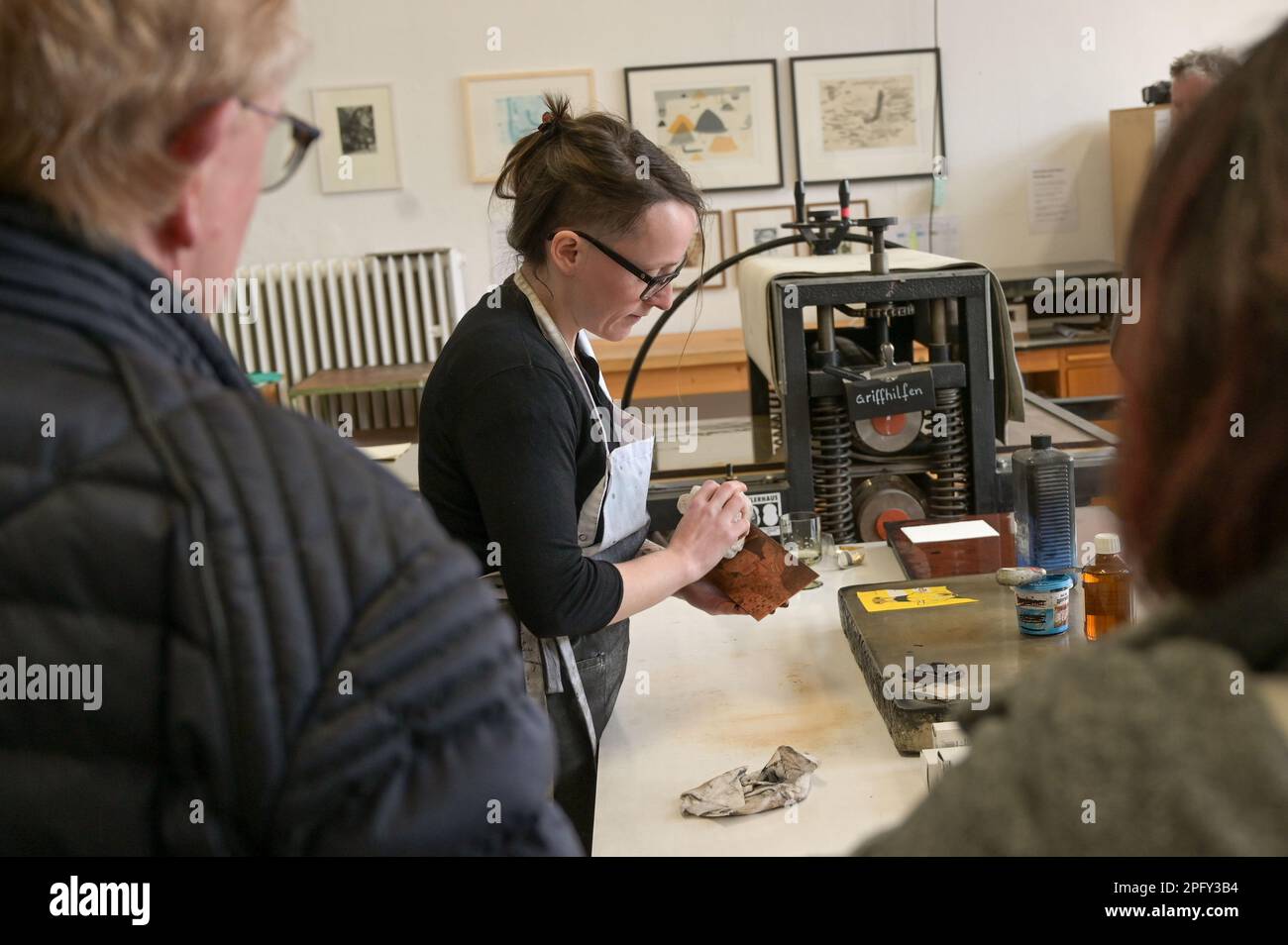 19. März 2023, Sachsen-Anhalt, Halle (Saale): Sarah Deibele (M) zeigt Besuchern die Technik der Ätzung, ein grafischer Intaglio-Prozess der künstlerischen Druckherstellung. Zum Tag der Druckherstellung hat das Künstlerhaus 188 Besucher zu Workshops, Druckvorführungen, Führungen und einer Ausstellung zum Thema Drucken eingeladen. Foto: Heiko Rebsch/dpa Stockfoto