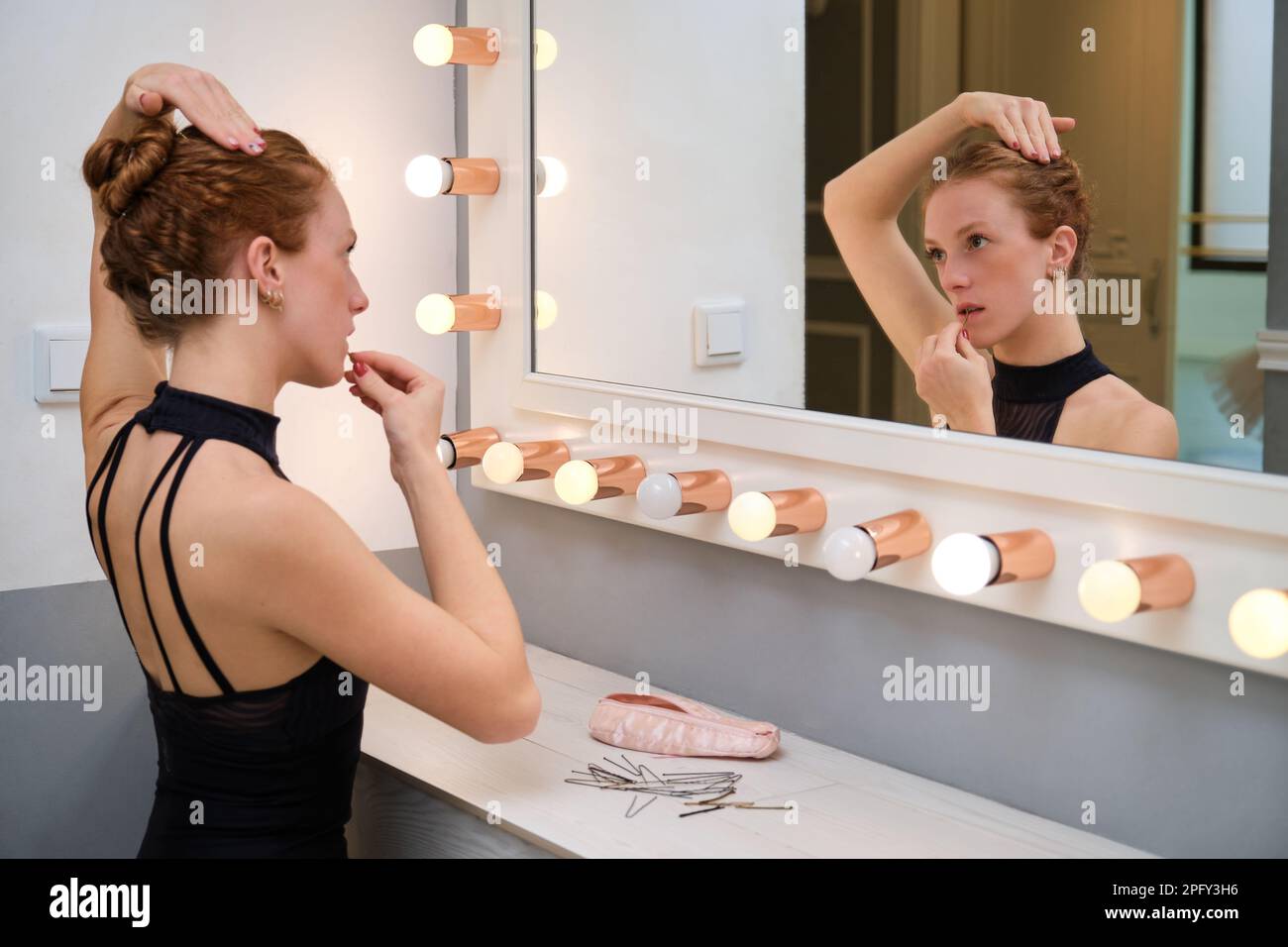 Junge Ballerina, die ihr Haar mit haarnadeln in ein Brötchen frisiert. Stockfoto