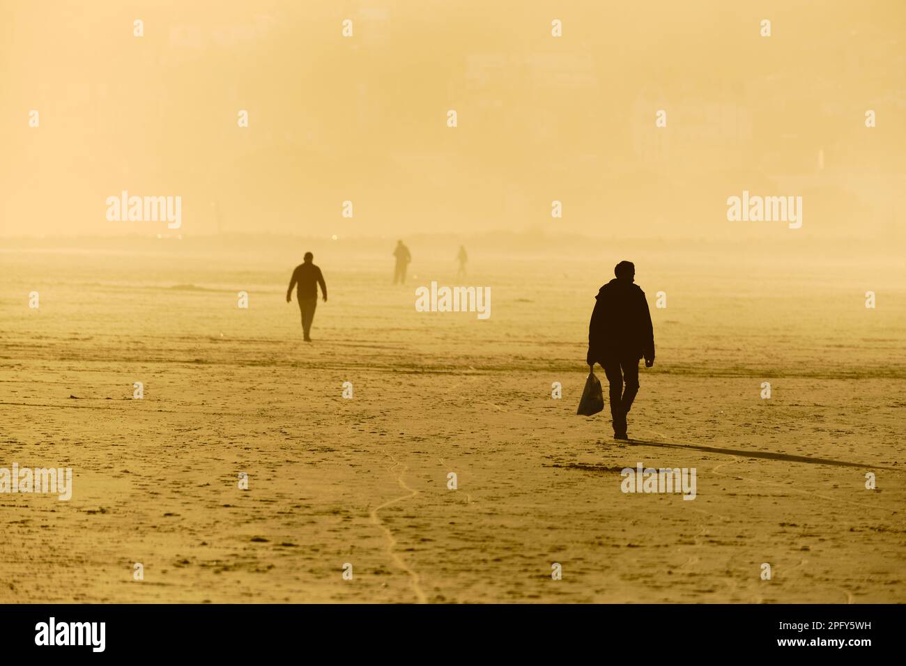 Menschen, die während der goldenen Stunde am Strand entlang spazieren, Bilder, die durch Sonnenlicht golden und Silhouetten gegen das Licht Stockfoto