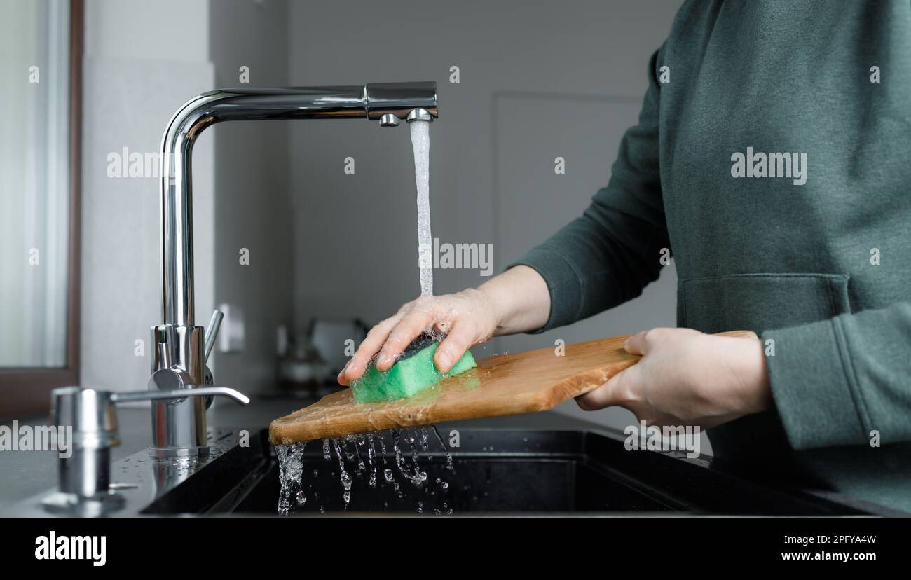 Frau wäscht Holzschneidebrett unter Wasser im Waschbecken in der Küche, reinigt zu Hause, kein Gesicht Stockfoto