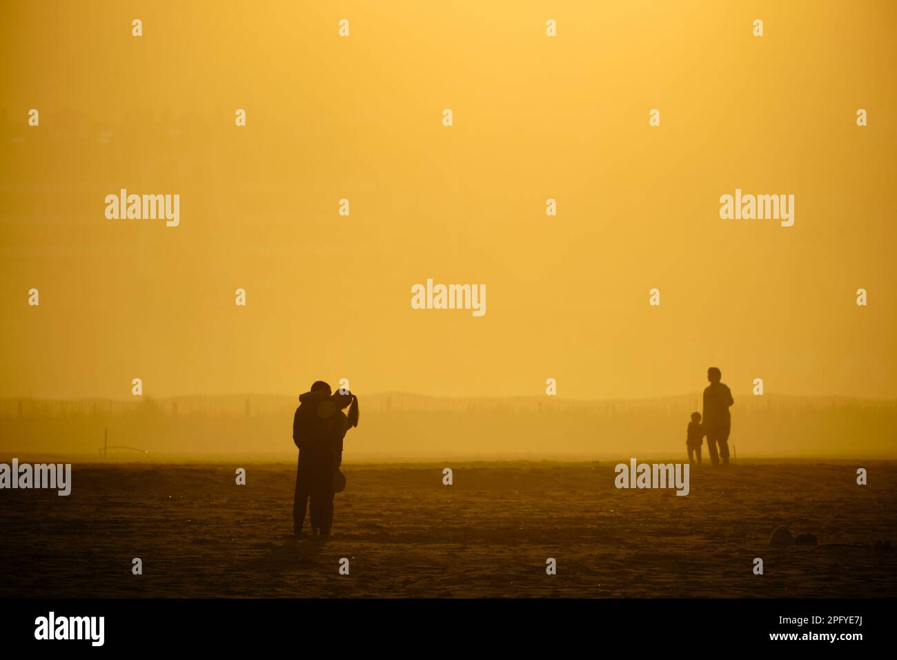 Menschen, die während der goldenen Stunde am Strand entlang spazieren, Bilder, die durch Sonnenlicht golden und Silhouetten gegen das Licht Stockfoto