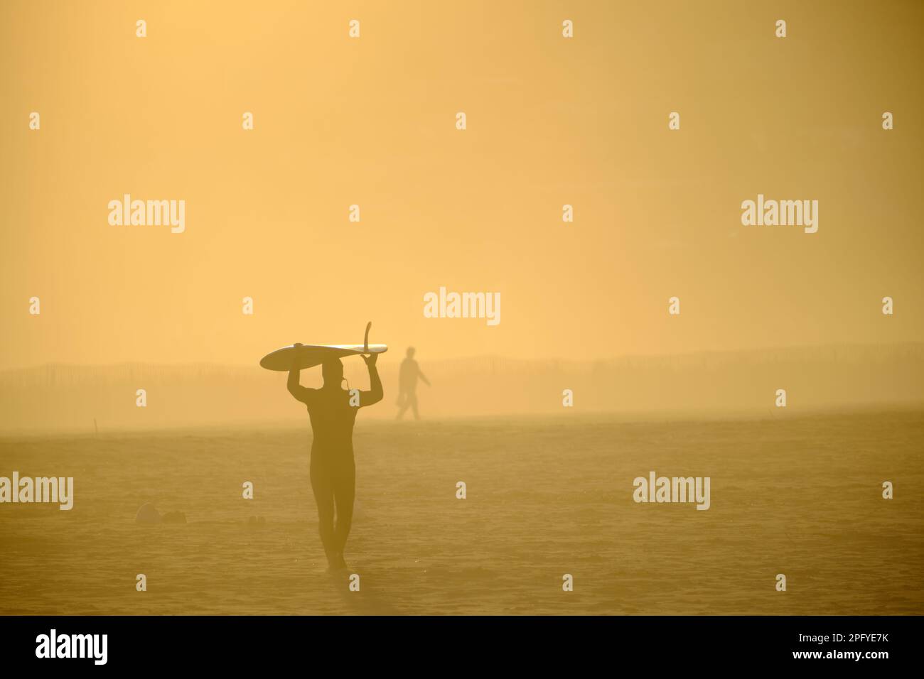 Menschen, die während der goldenen Stunde am Strand entlang spazieren, Bilder, die durch Sonnenlicht golden und Silhouetten gegen das Licht Stockfoto