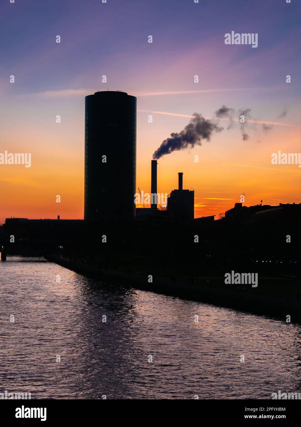 Silhouetten eines runden Wolkenkratzers und eines Industriegebäudes am Ufer des Main in Frankfurt bei Sonnenuntergang Stockfoto