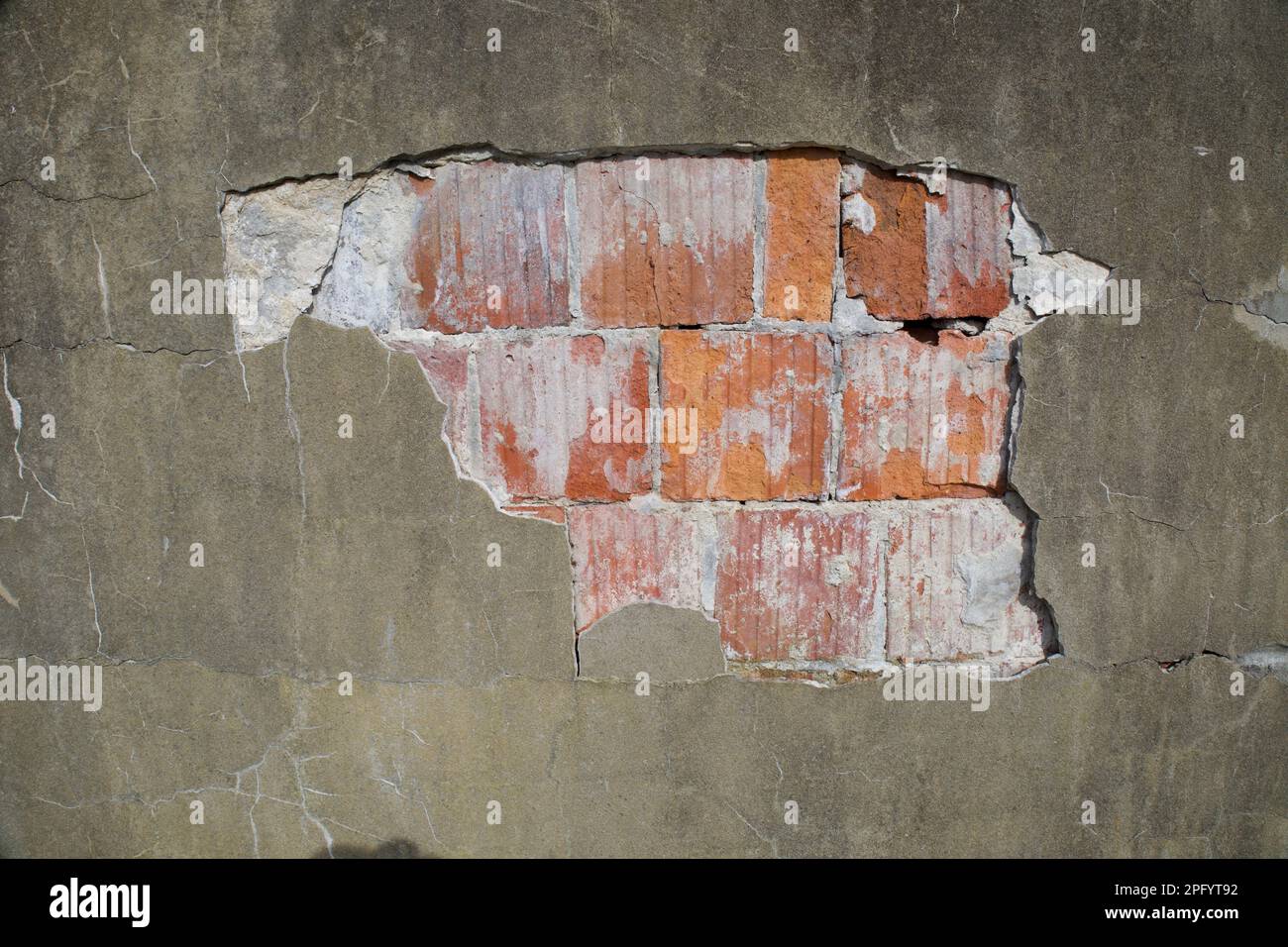 Details einer freiliegenden Betontrennwand, die auseinanderfällt, Risse und Löcher in der Wand. In der Wand ist roter Ziegel. Stockfoto