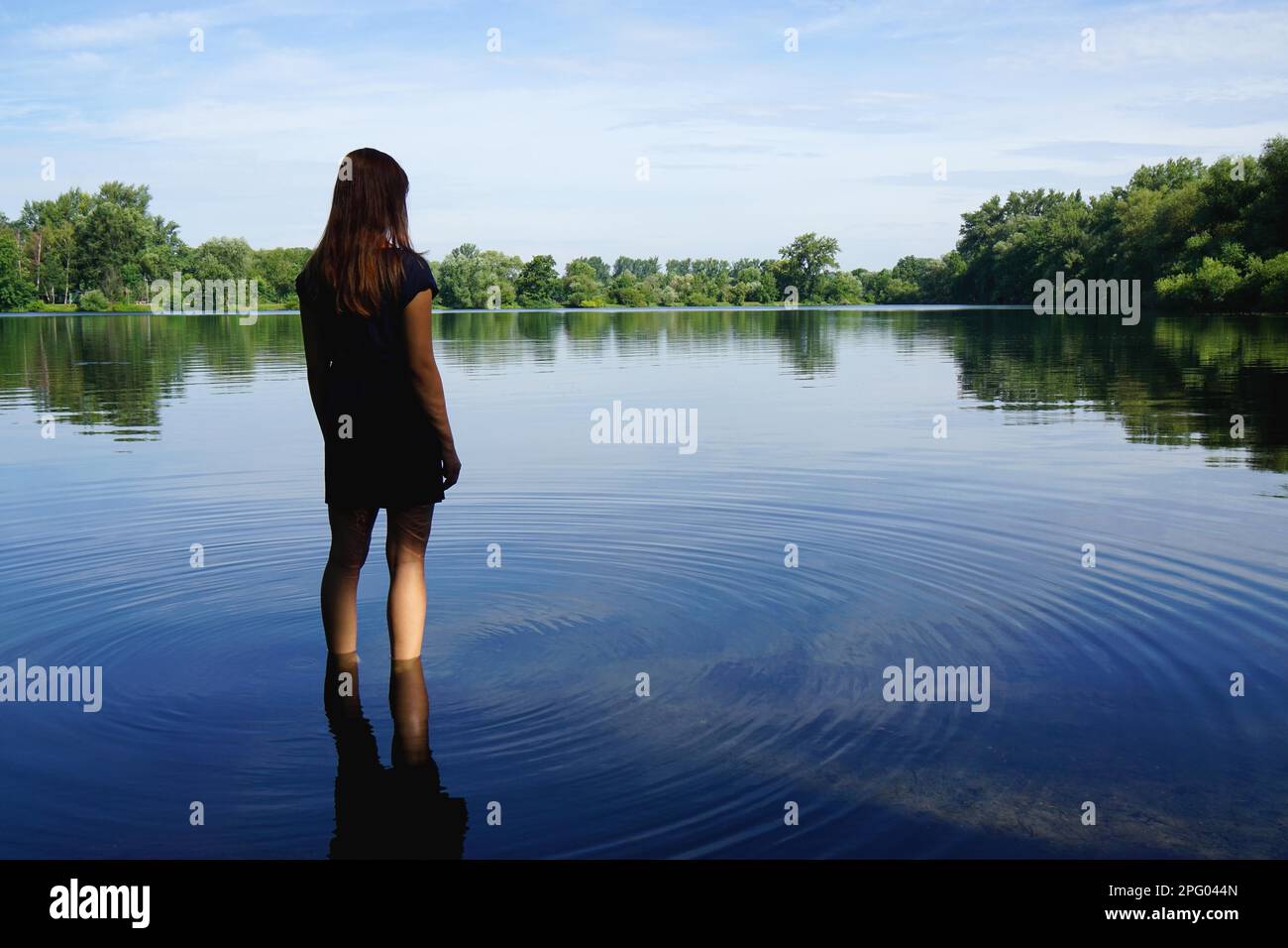 Rückblick einer jungen Frau, die in Einsamkeit im See steht Stockfoto
