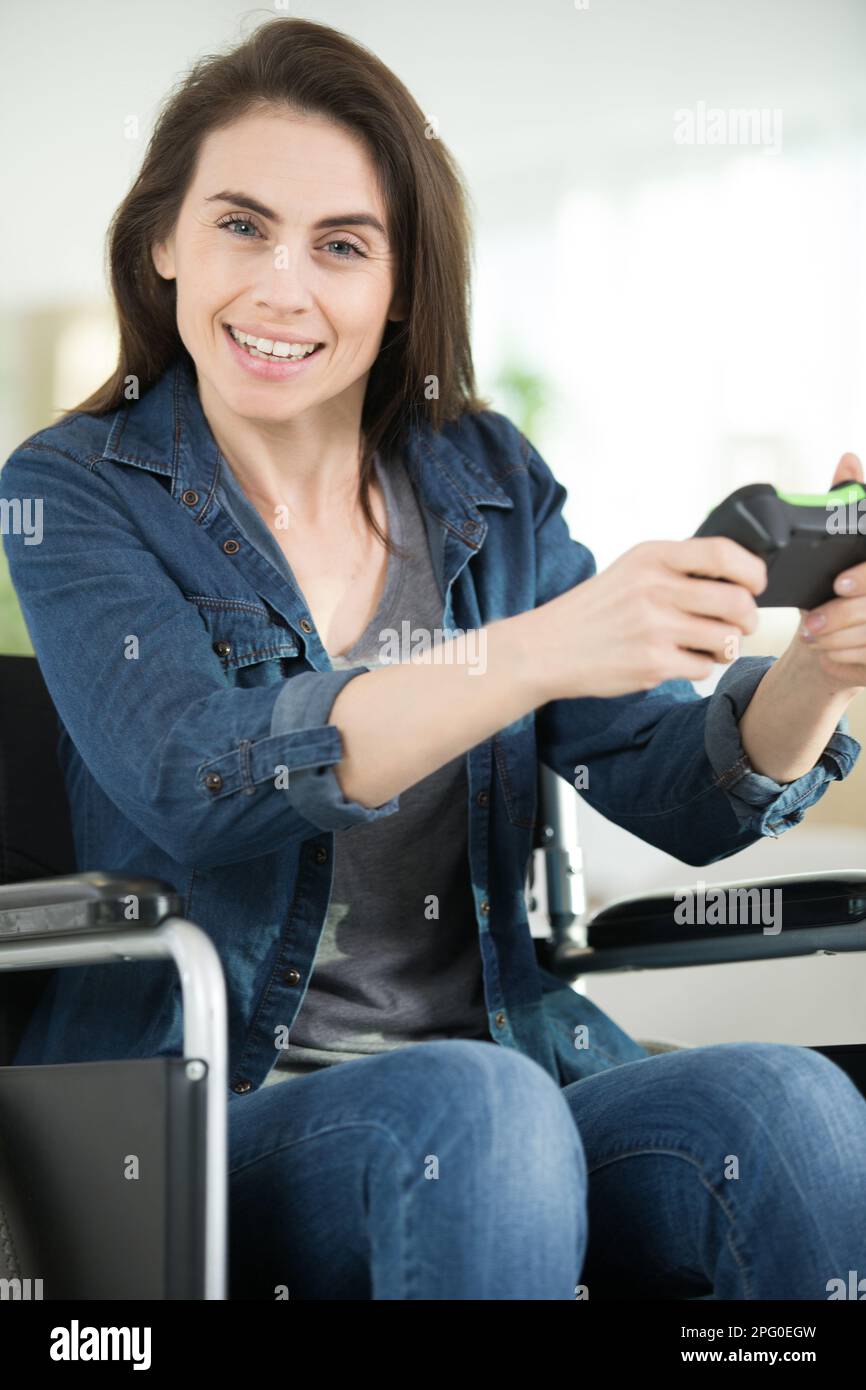 Glückliche, behinderte Frau, die in die Kamera schaut, während sie den Controller benutzt Stockfoto
