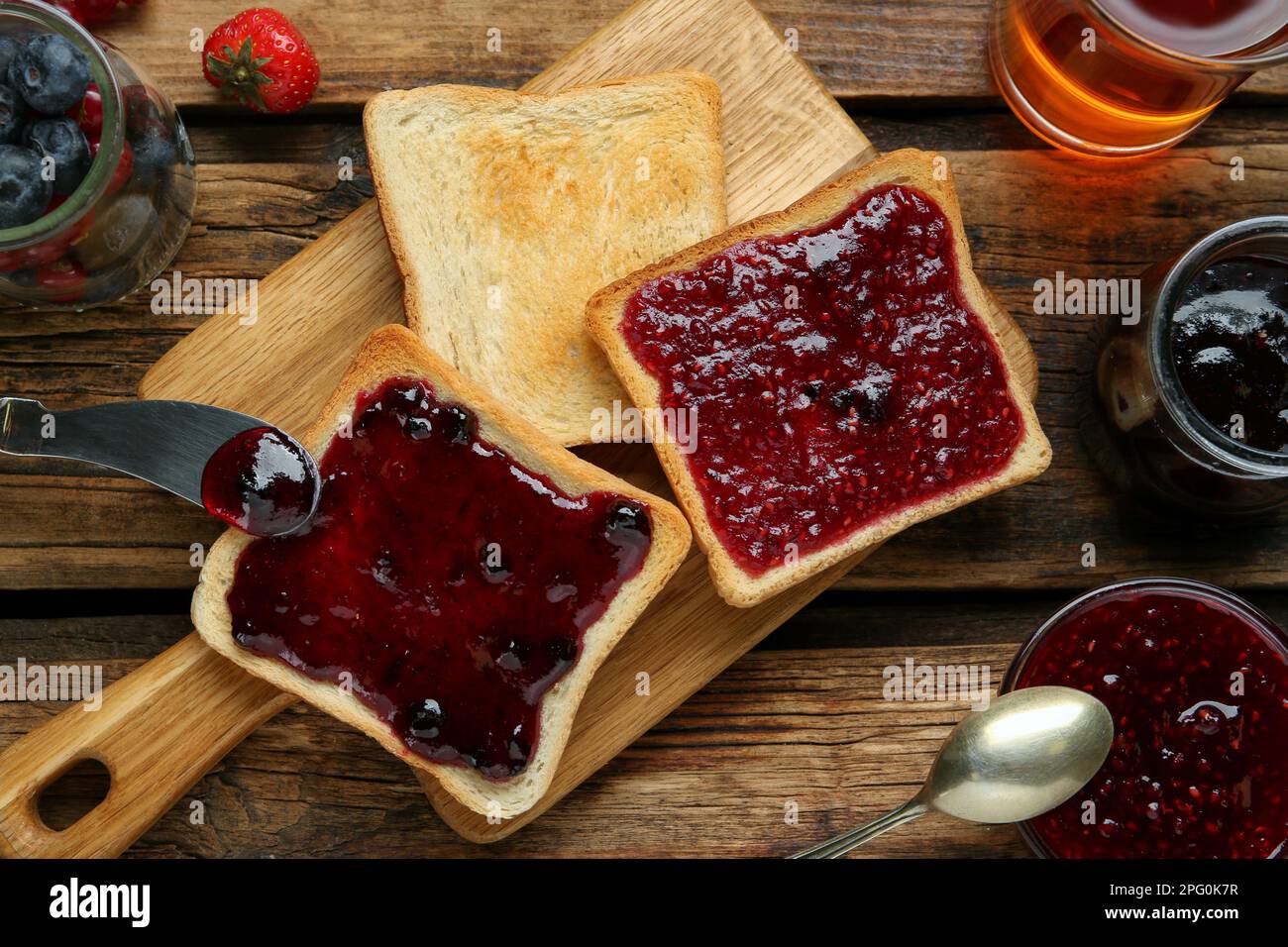 Köstliche Toasts mit verschiedenen Marmeladen, Tee und Beeren auf einem Holztisch, flach liegend Stockfoto