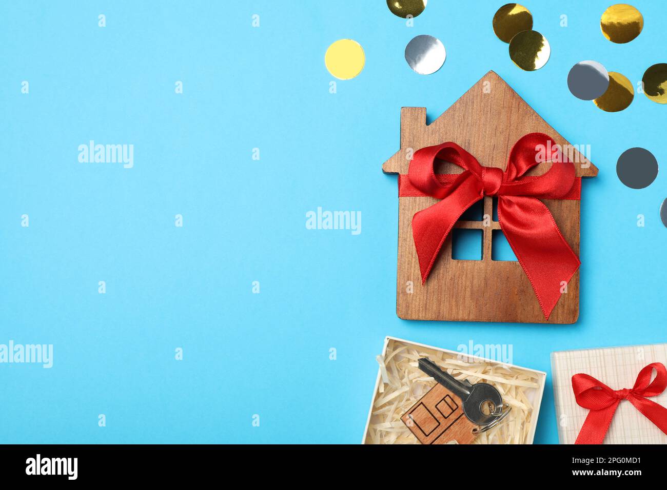 Hausmodell aus Holz und Schlüssel in Geschenkbox auf hellblauem Hintergrund, flach liegend mit Platz für Text. Einweihungsparty Stockfoto