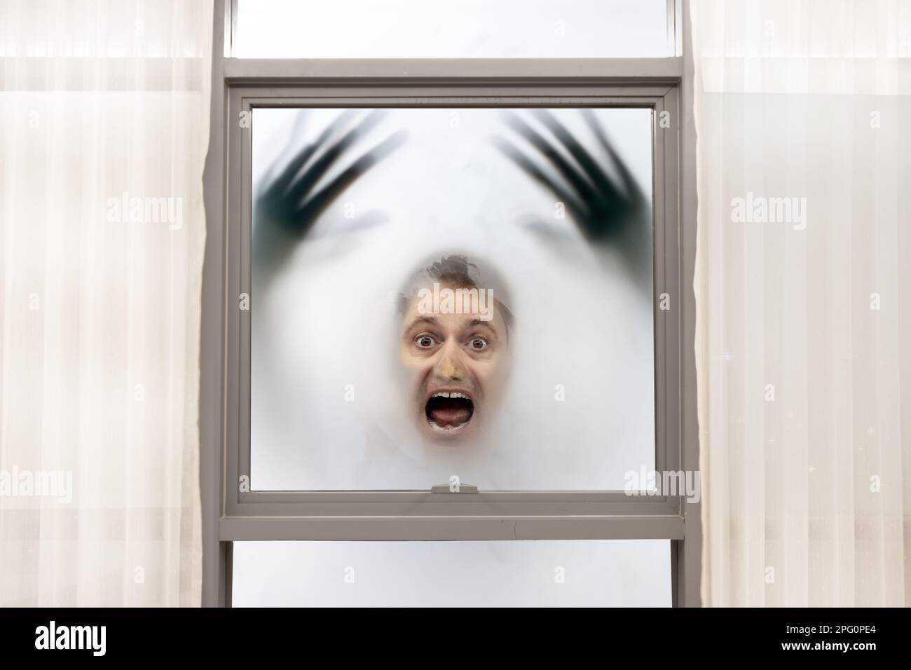 Schreiender Mann mit verschwommenen Händen hat sein Gesicht gegen das Fenster gedrückt auf einem nebligen Hintergrund Stockfoto