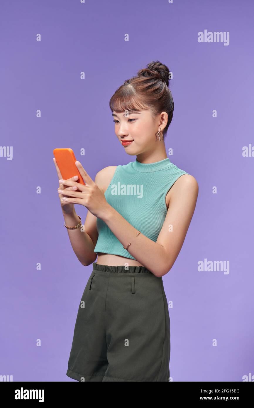 Lächelndes junges Mädchen, das ein Smartphone mit drahtloser Verbindung verwendet, isoliert auf lila Stockfoto