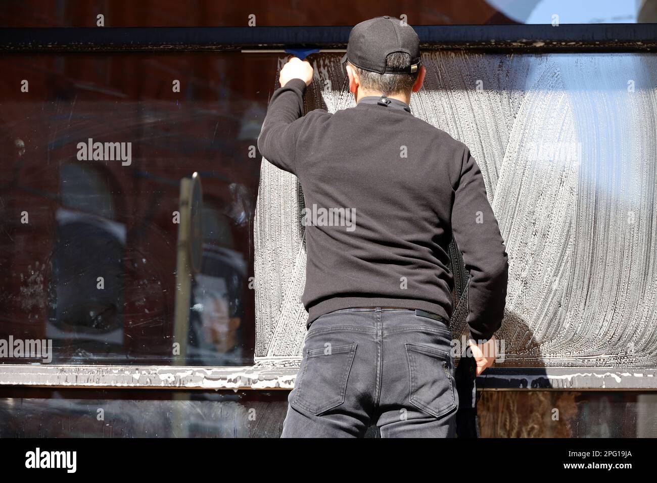Fensterputzer, männlicher Arbeiter wäscht das Glas der Straßencafe Fassade. Reinigung in der Frühlingsstadt Stockfoto