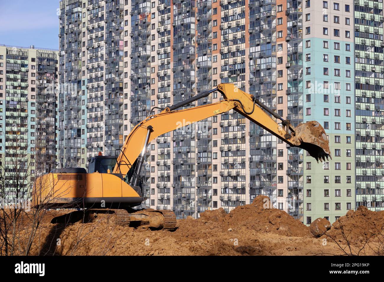 Raupenbagger schaufeln die Erde mit einem Löffel auf dem Hintergrund neuer Wohngebäude. Erdbewegungsarbeiten, Grabarbeiten und Bauindustrie Stockfoto