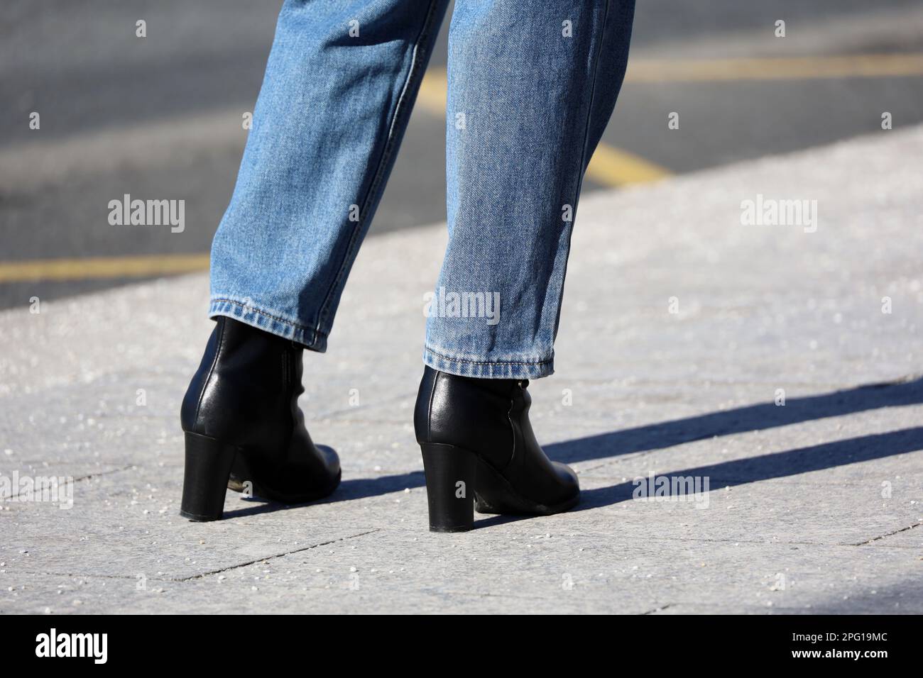 Weibliche Beine in schwarzen Schuhen auf hohen Absätzen auf gepflastertem Bürgersteig. Mädchen trägt Jeans auf der Straße, Mode in Spring City Stockfoto