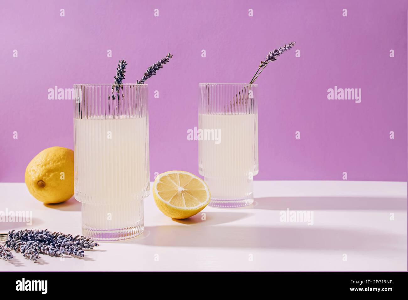 Zwei gerippte Gläser mit Lavendel-Limonade auf violettem Hintergrund, erfrischendes Sommergetränk Stockfoto