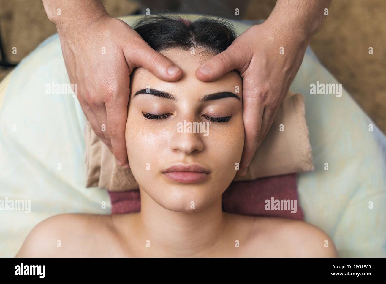 Der Spezialist macht eine entspannende Massage der Gesichtsmuskulatur an eine weibliche Klientin, eine Nahaufnahme des Gesichts von oben Stockfoto
