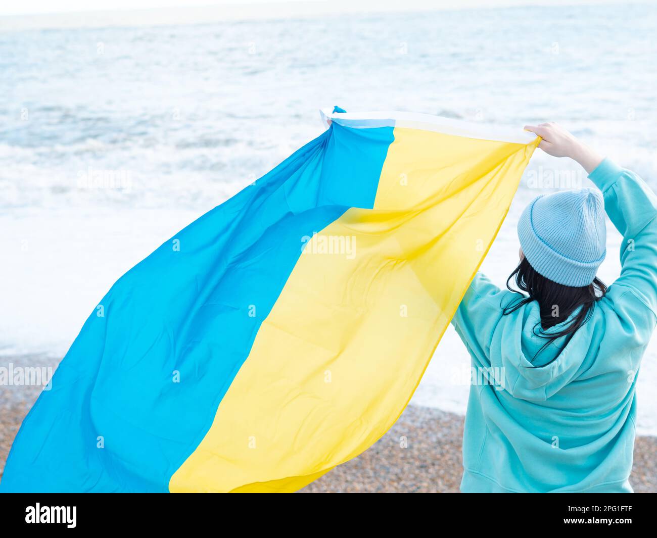 Braune Frau in blauem Hoodie und blauem Hut mit ukrainischer Nationalflagge, patriotisches Konzept Stockfoto