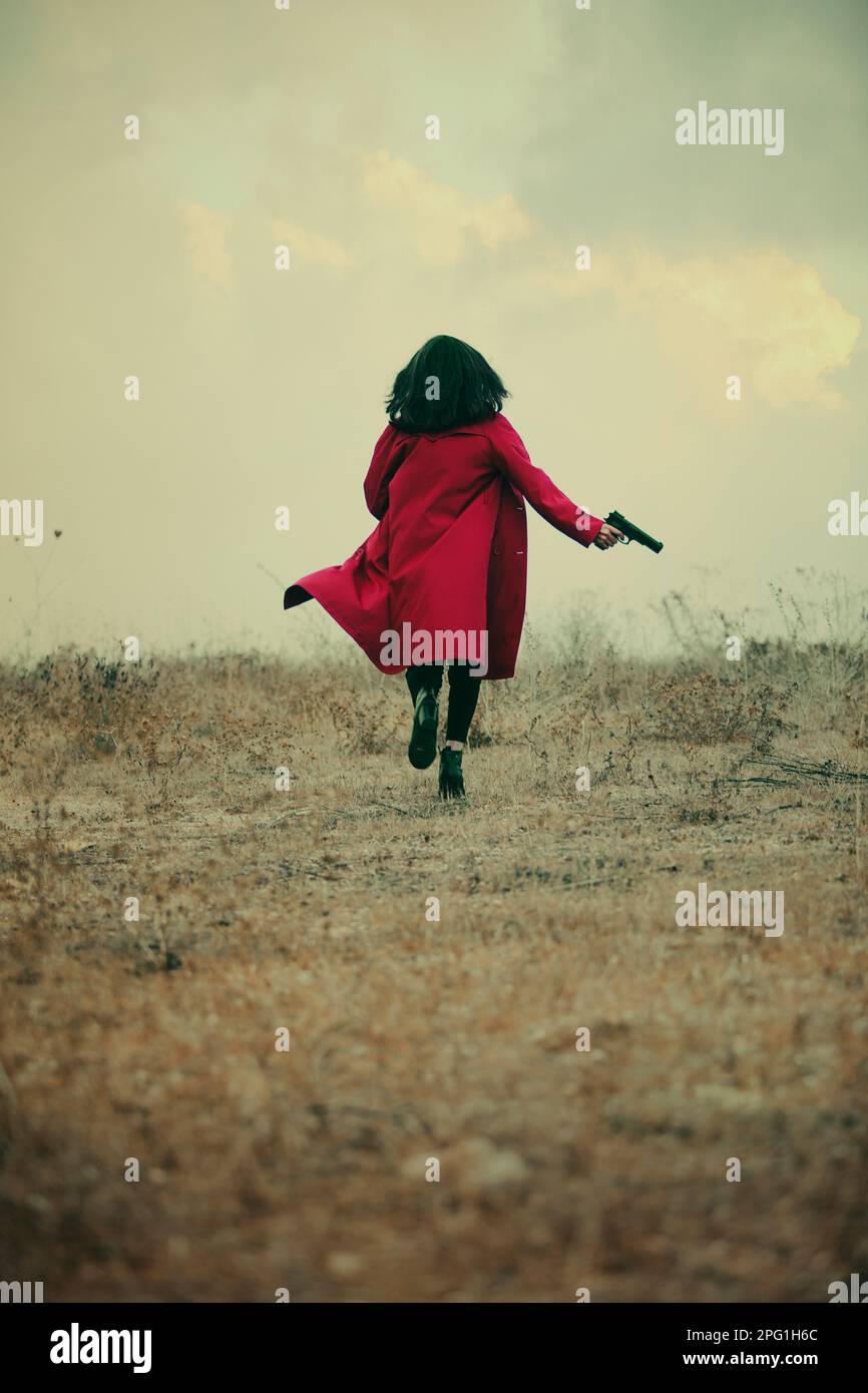 Eine Frau in rotem Mantel, die mit einer Waffe davonläuft Stockfoto