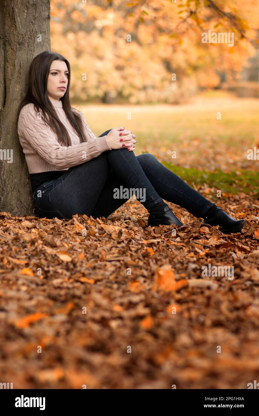 Traurige, schöne Frau saß am Baum und schaute weg Stockfoto
