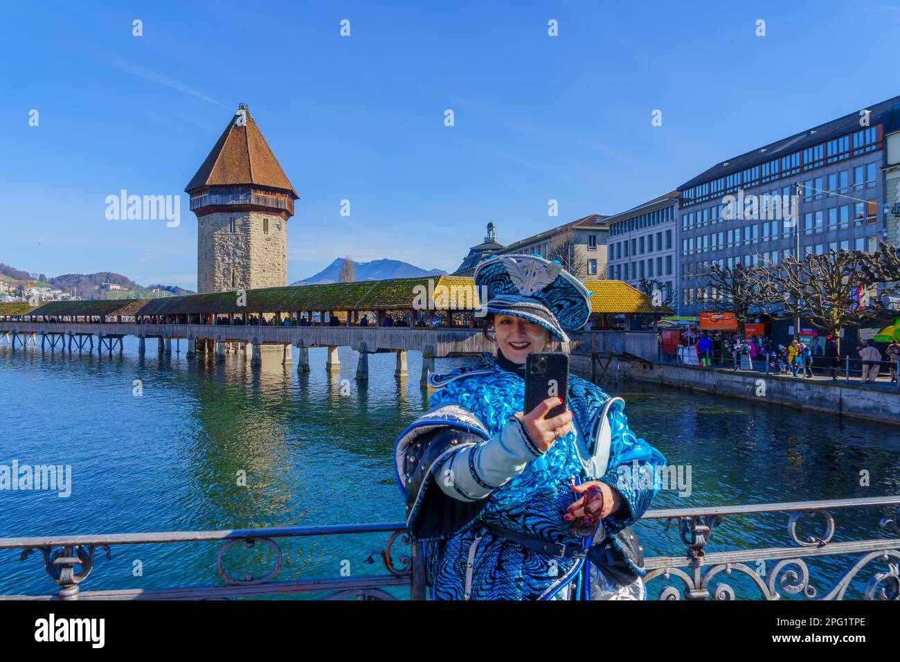 Luzern, Schweiz - 20. Februar 2023: Kostümteilnehmer machen Selfie, Menge und Stadtdenkmäler im Hintergrund, Teil der Fasnacht Carn Stockfoto