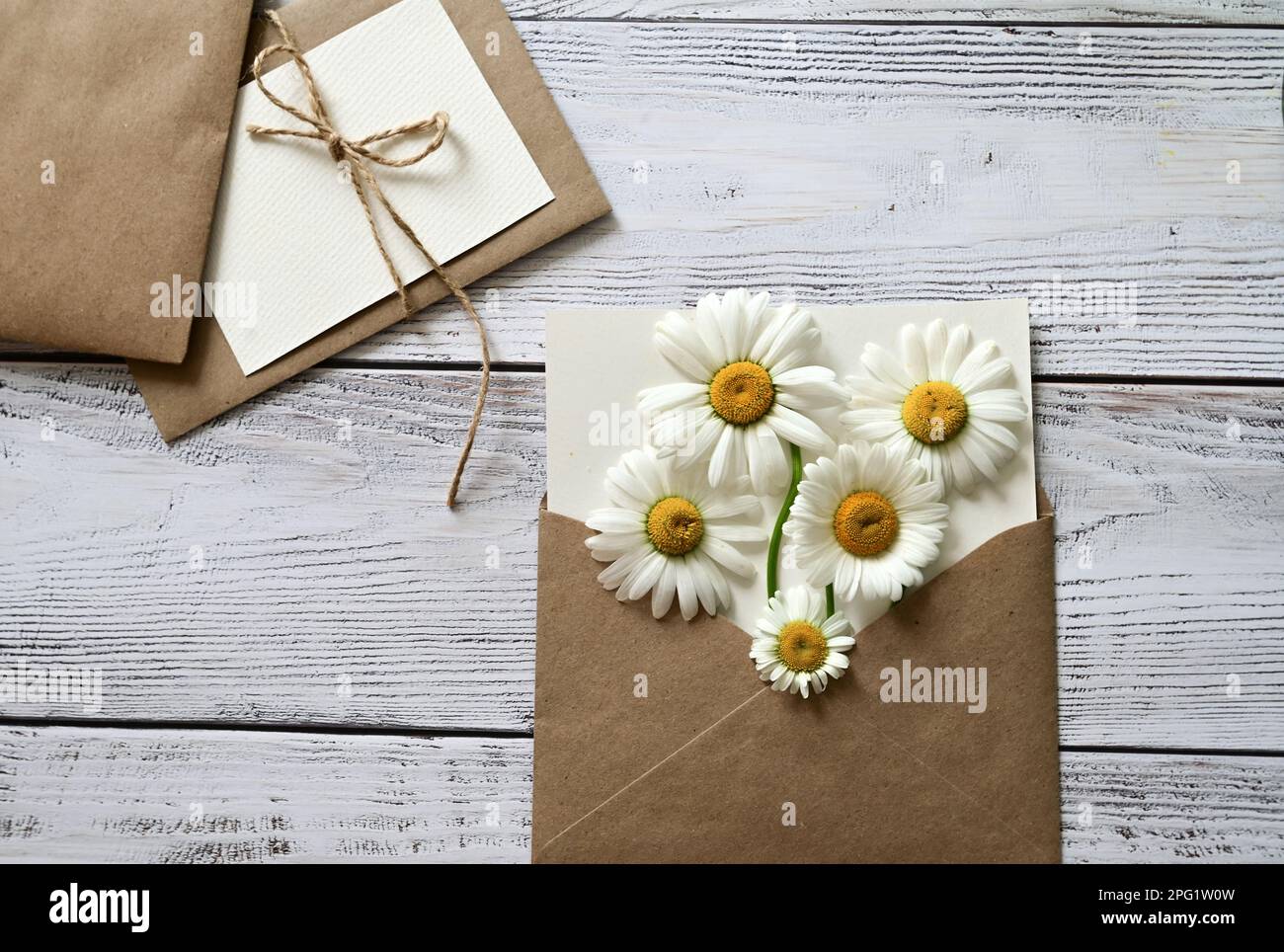 Eine leere Grußkarte mit einem braunen Umschlag und einer weißen Blume für die mutter auf einem Holztisch im Vintage-Stil und mit Vignetten Stockfoto