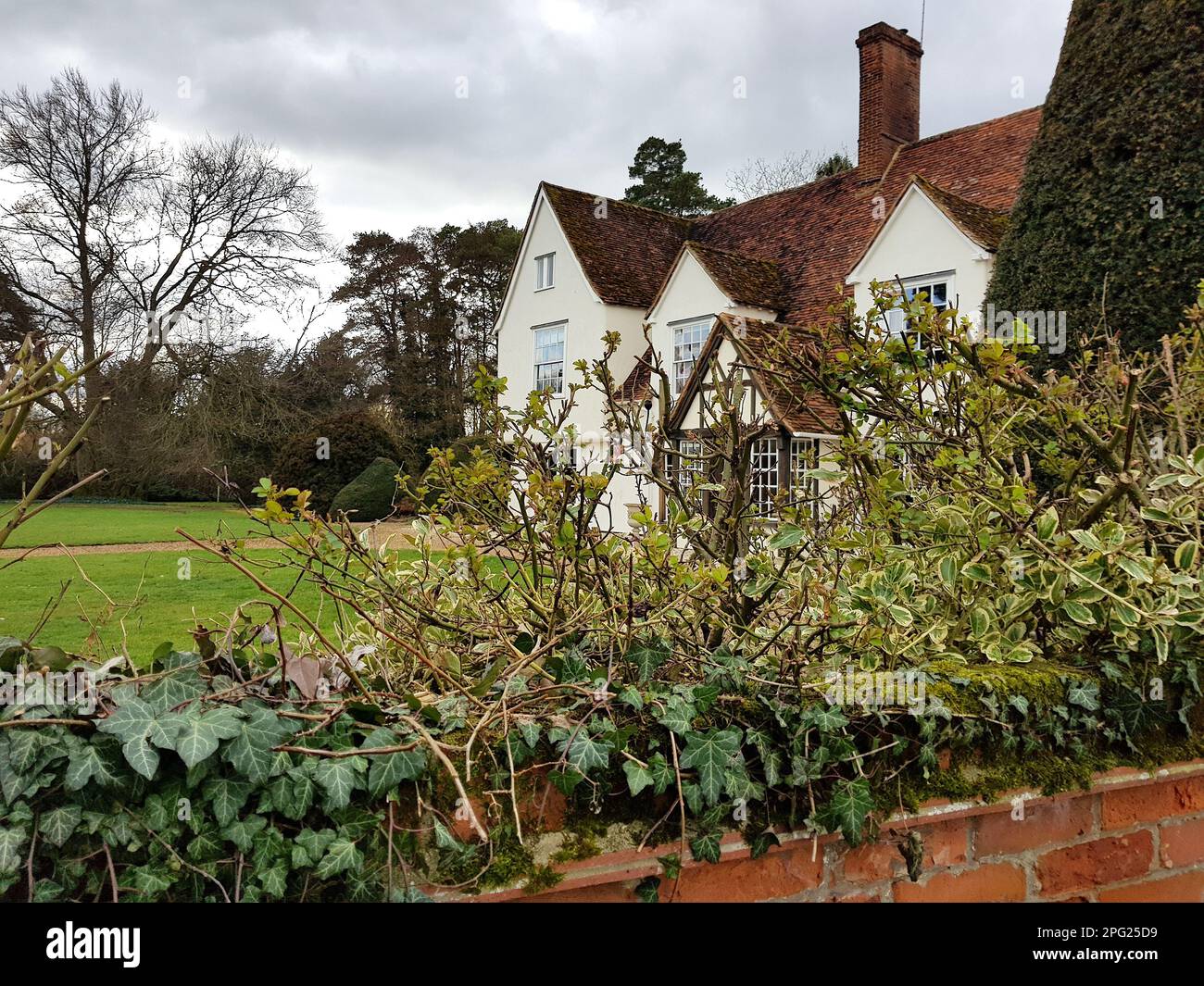 Ein historisches Bauernhaus mit einer roten Backsteinwand im Vordergrund in Essex, Großbritannien. Stockfoto