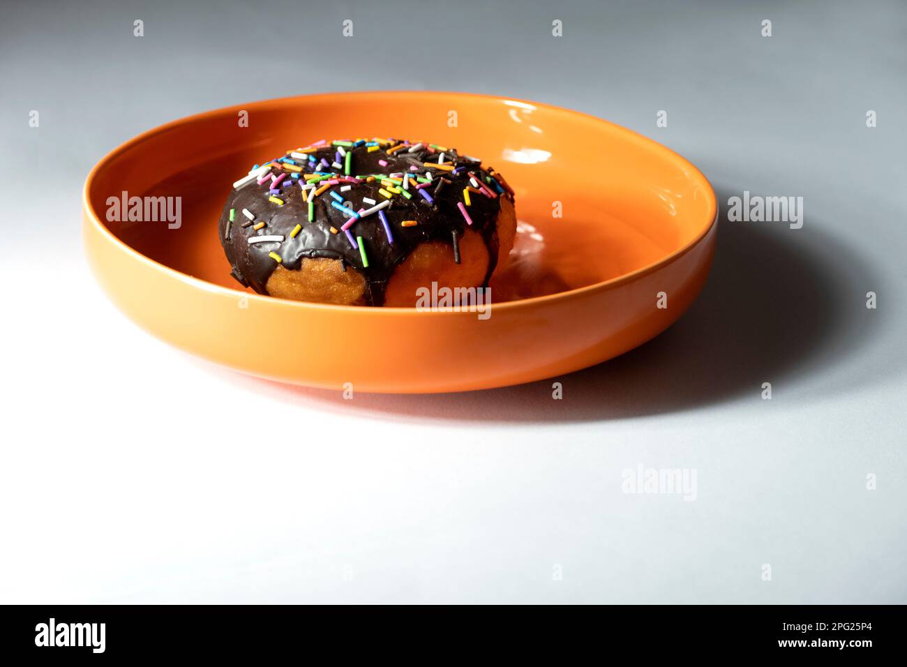 Bunte Donuts auf orangefarbener Platte auf weißem Hintergrund. Stockfoto