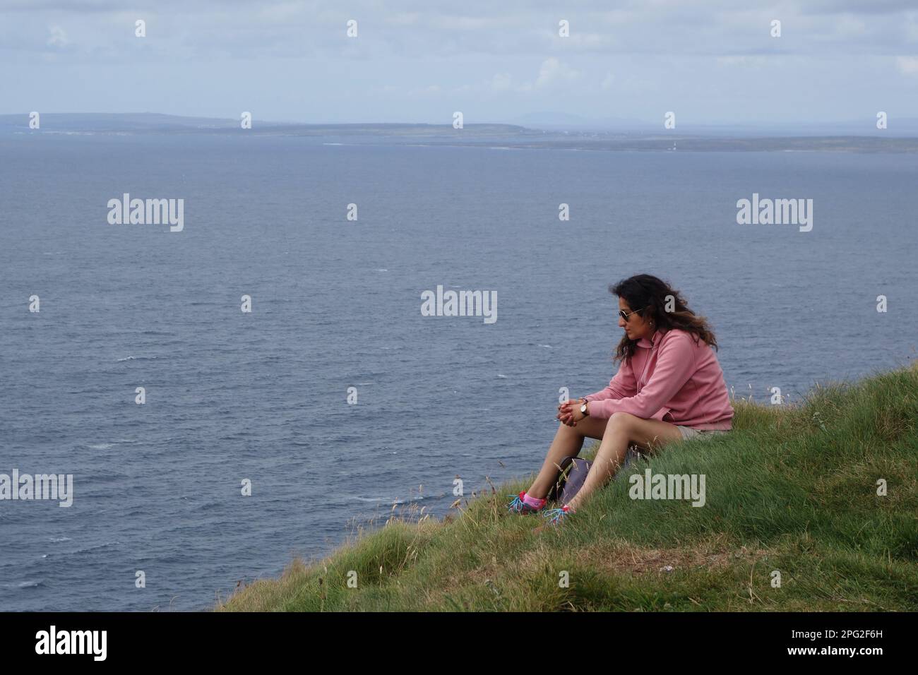 Junge Frau, die sich am Klippenrand in Cliffs of Moher, irland, erholt Stockfoto