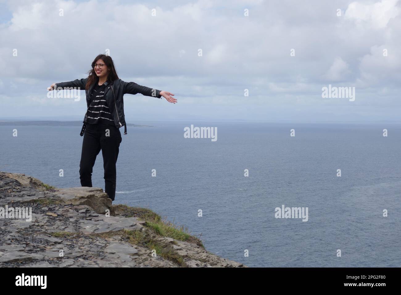 Junge Frau, die am Klippenrand in Cliffs of Moher, irland, posiert Stockfoto