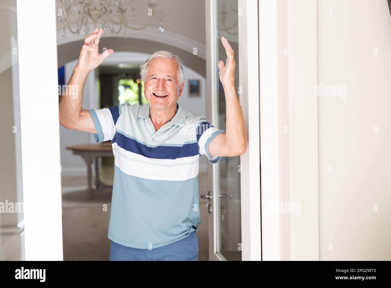 Porträt eines glücklichen Weißen Seniorenmannes, der in die Kamera schaut und an der Tür begrüßt wird Stockfoto