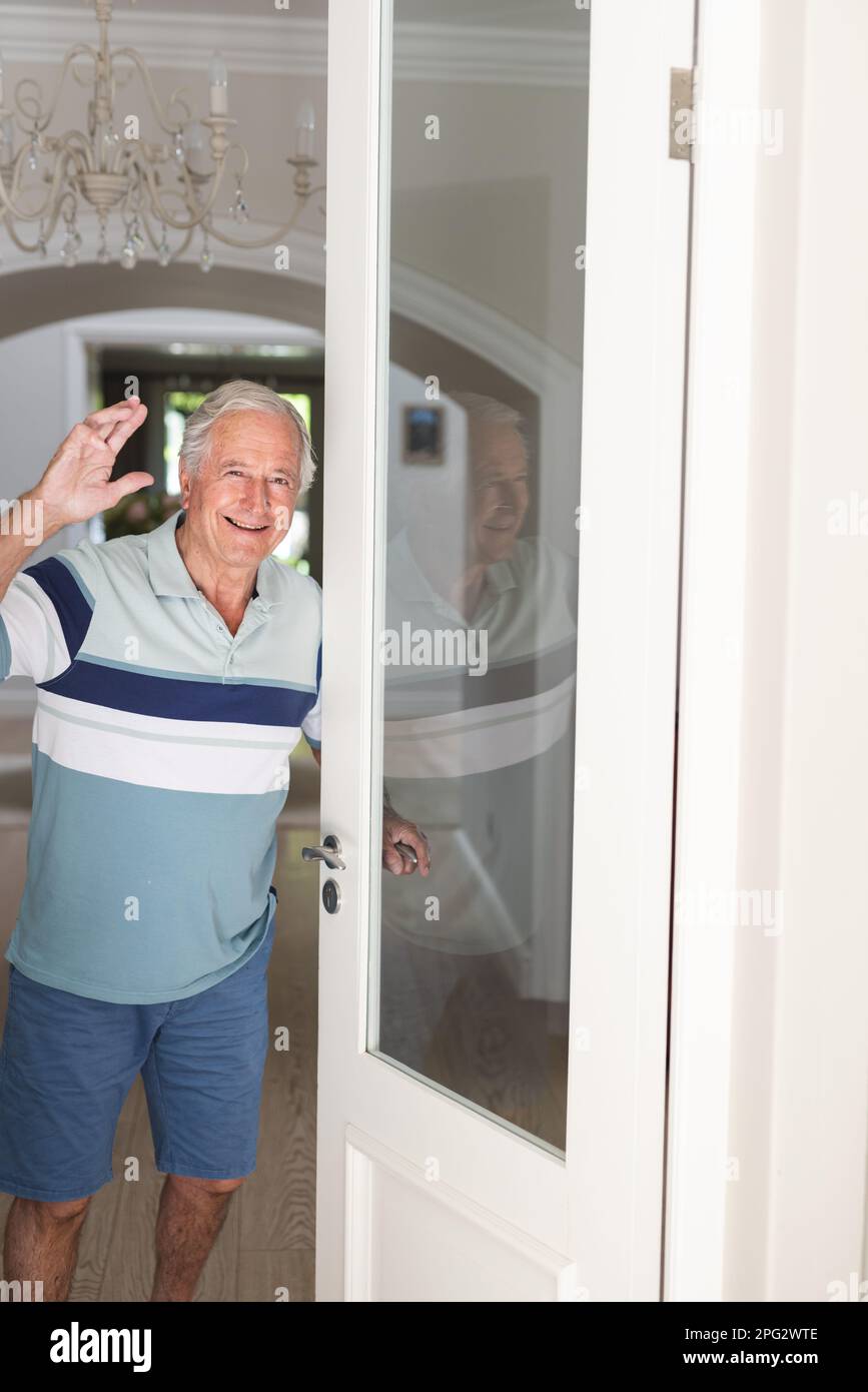 Porträt eines glücklichen Weißen Seniorenmannes, der in die Kamera schaut und an der Tür begrüßt wird Stockfoto