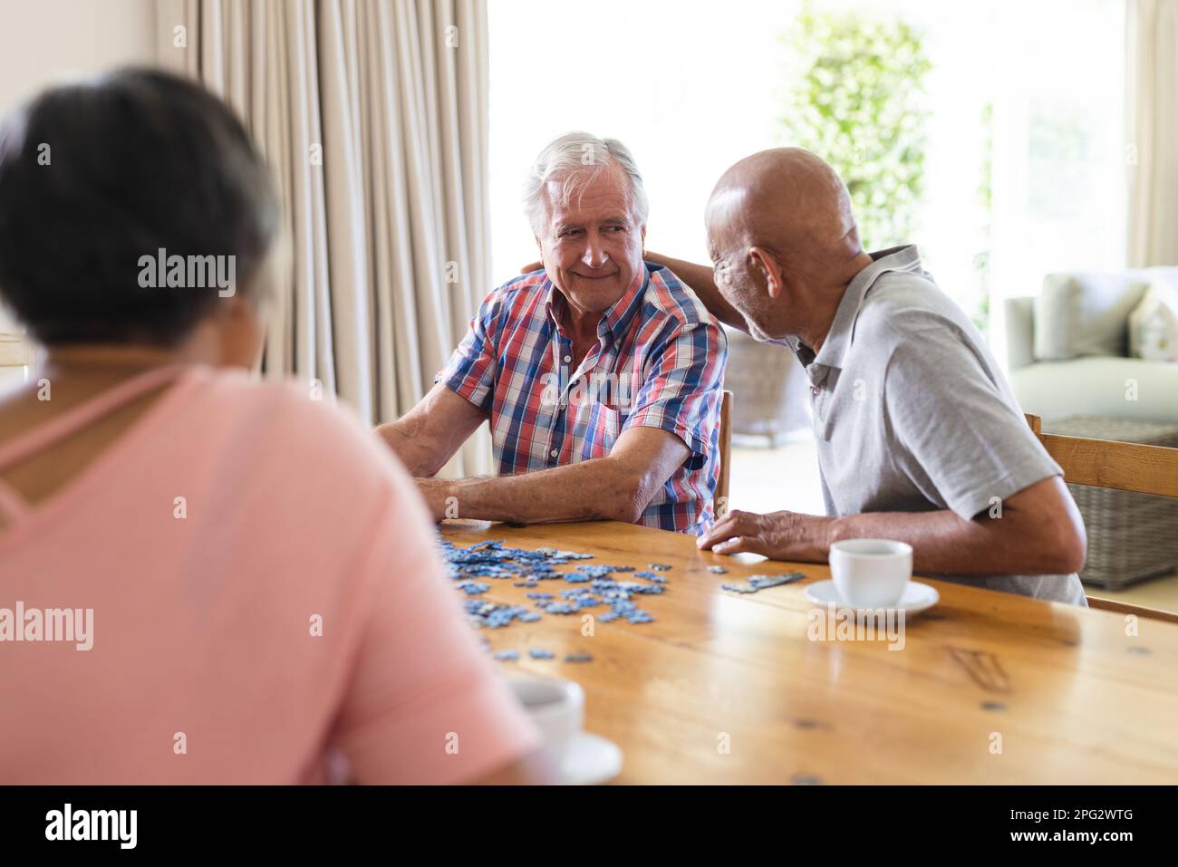 Eine glückliche Gruppe verschiedener Senior-Freunde, die am Tisch sitzen und Puzzle spielen Stockfoto