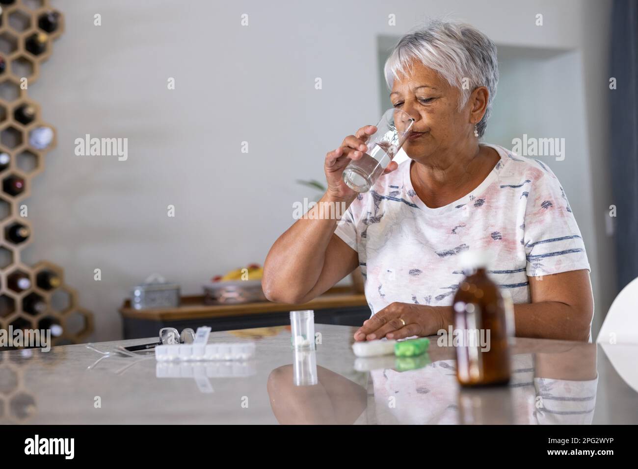 Birassische Seniorin mit grauen kurzen Haaren, die zu Hause verschriebene Medikamente und Trinkwasser einnimmt Stockfoto