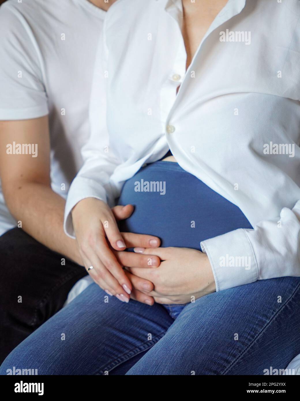 Eine Nahaufnahme der miteinander verbundenen Hände eines liebevollen Paares, das auf dem Bauch einer schwangeren Frau ruht Stockfoto