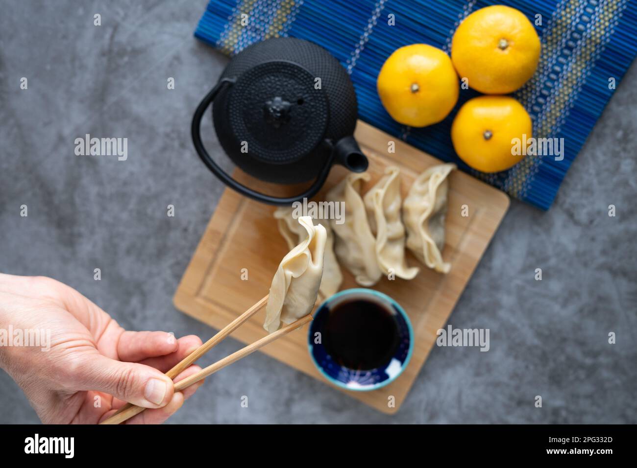 Asiatisches Essen. Nimm mit der Hand Lebensmittel mit Essstäbchen auf. Dim Sum mit Sojasoße auf Bambusbrett mit Orangen und Teekanne. Speicherplatz kopieren. Draufsicht. Stockfoto