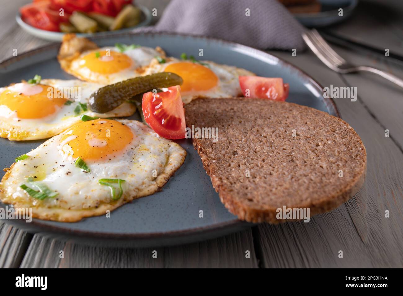 Spiegeleier, sonnige Seite nach oben mit Roggenbrot, Tomaten und Gurken. Traditionelle deutsche, rustikale Mahlzeit Stockfoto
