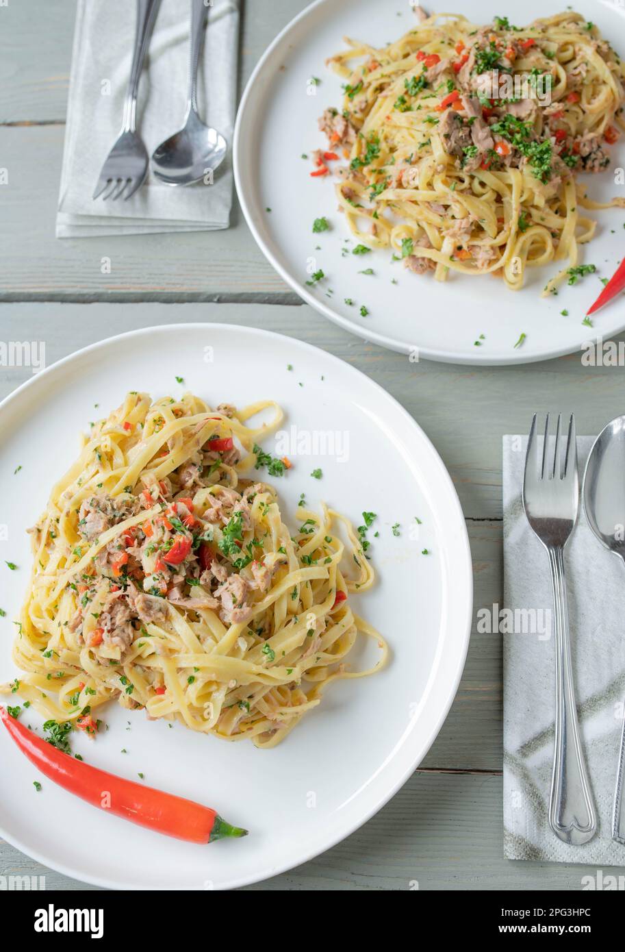 Italienisches Nudelgericht „aglio e olio“. Tagliatelle-Nudeln mit Olivenöl, Knoblauch, Petersilie und Chili-Paprika. Mit Thunfisch zubereitet und auf Tellern serviert Stockfoto