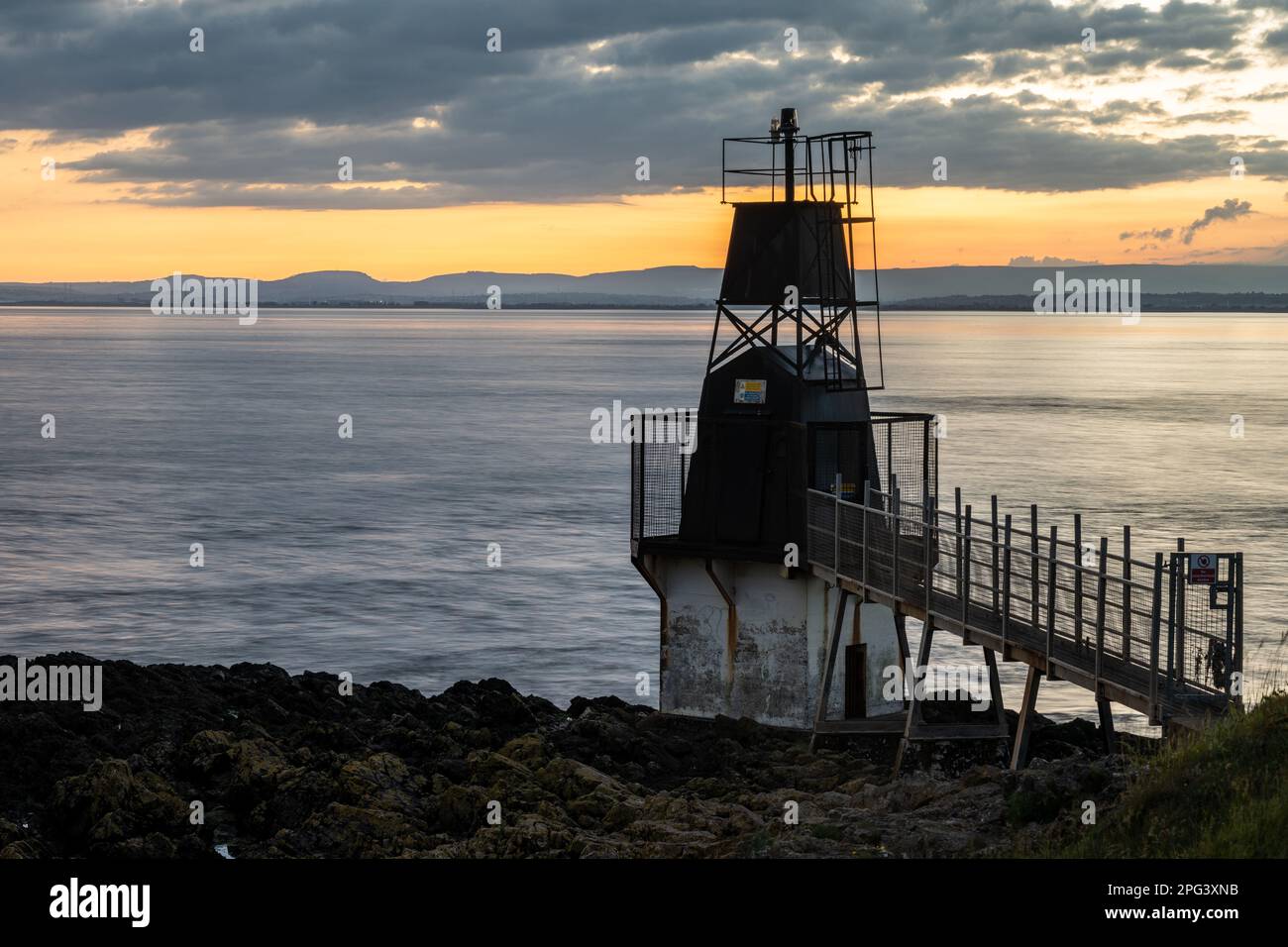 Die Sonne geht über dem Battery Point Lighthouse in Portishead am Bristol Channel unter, mit den Hügeln von Südwales dahinter. Stockfoto