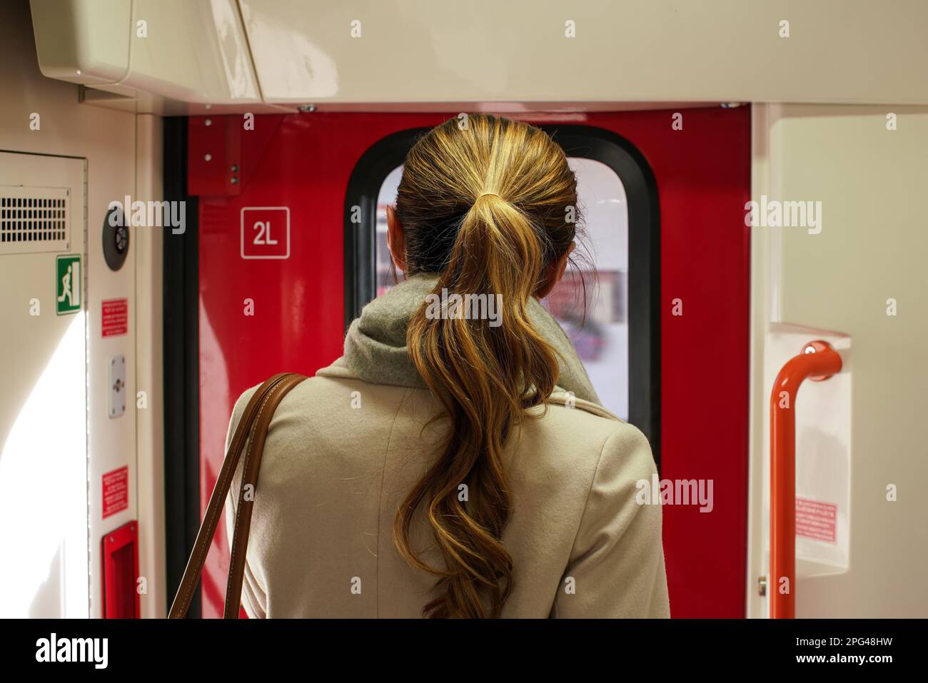 Junge Frau im Mantel, die neben der Tür stand, die den Zug stoppte und gleich wieder verlassen wollte - Blick von hinten Stockfoto
