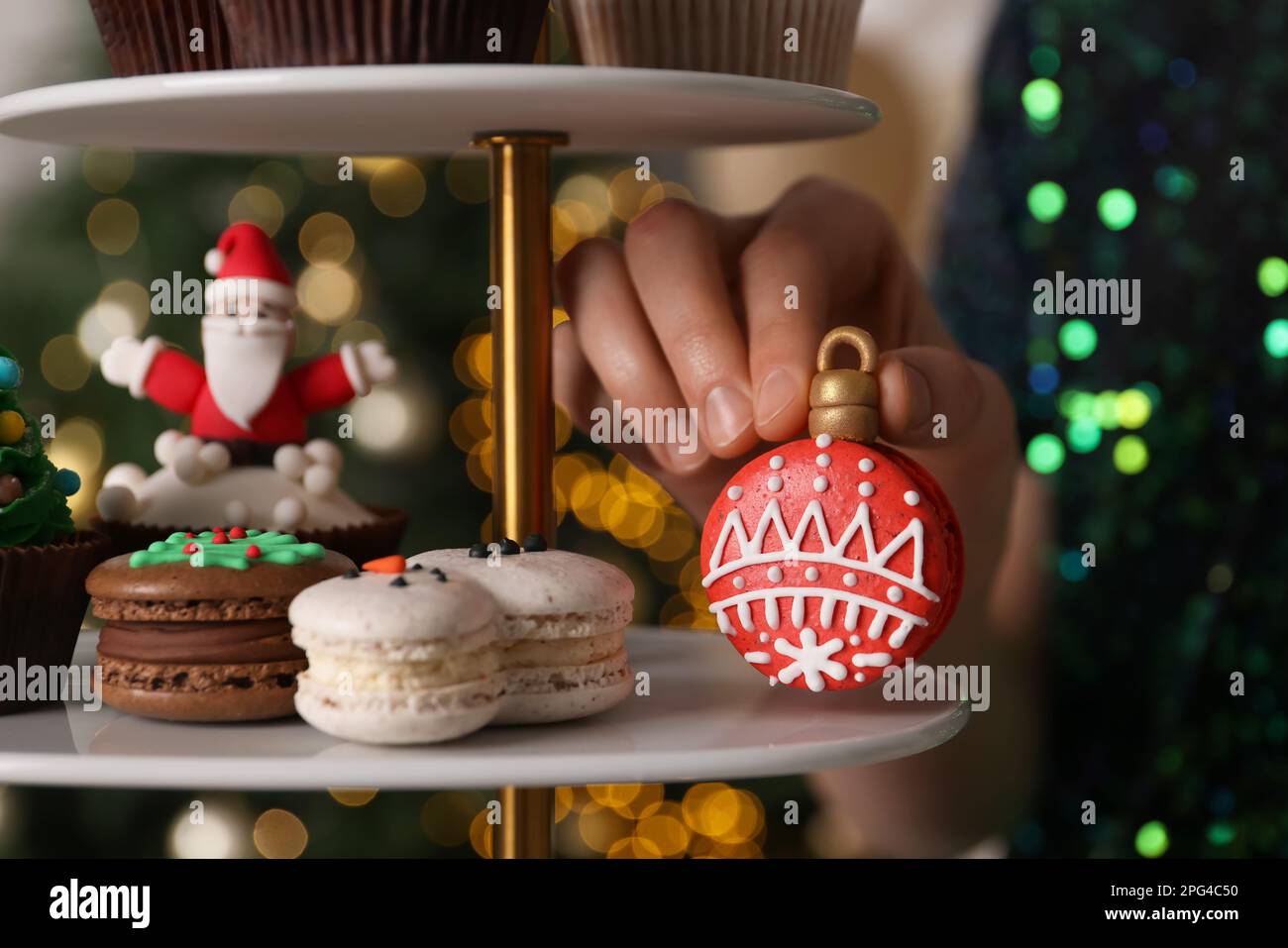 Eine Frau, die Weihnachtsmakaron aus dem Stand nimmt, gegen verschwommene festliche Lichter, Nahaufnahme Stockfoto