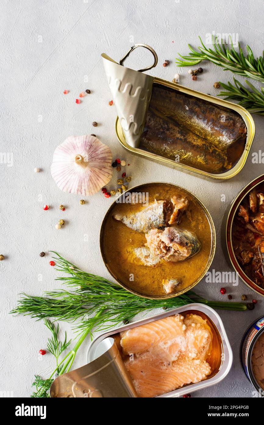 Verschiedene offene Blechdosen mit Fischkonserven unter Gewürzen und Kräutern, Lachs- und Makrelenkonserven, Sprotte und Sardine, Thunfisch und Hering sowie Fischpastete Stockfoto